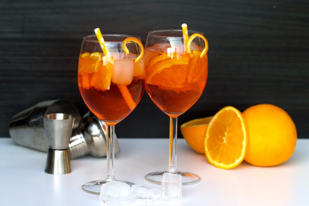 Two iced Aperol Spritz drinks, with a cut citrus next to them on the right.