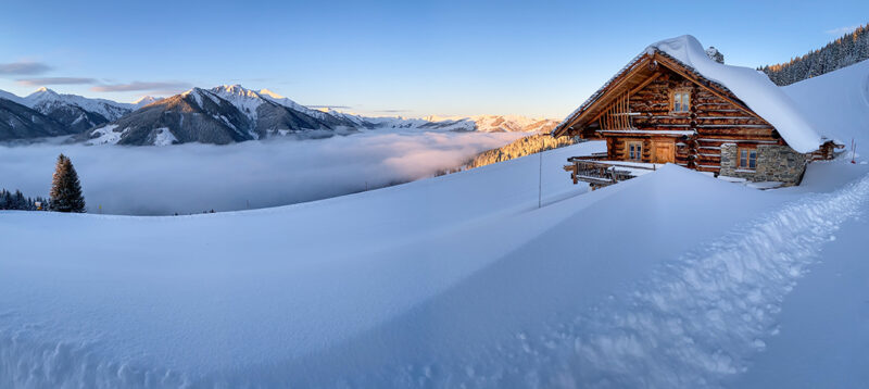 A snow-covered house sits in a white landscape with mountains rising in the background.