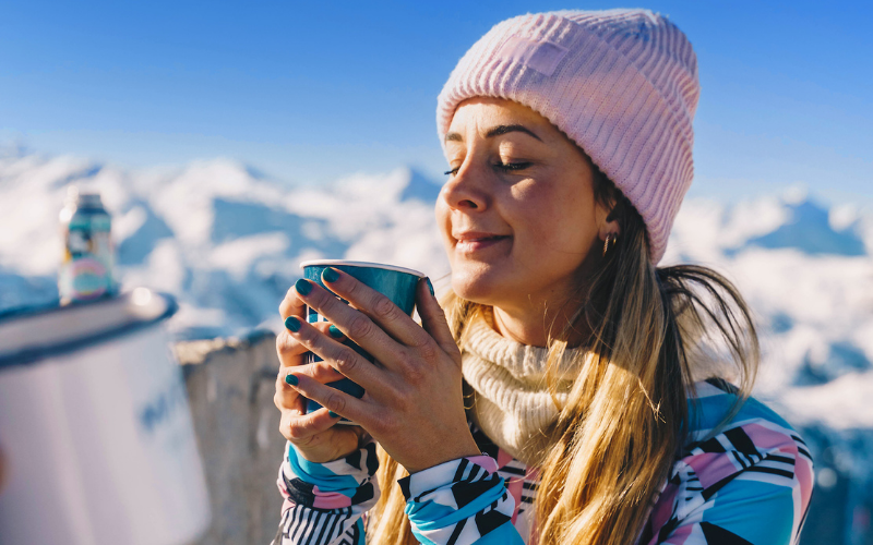 Woman enjoying the sunshine in the mountains, holding a drink.